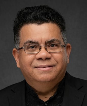 Professional headshot of a middle-aged man wearing glasses and a black shirt against a gray background