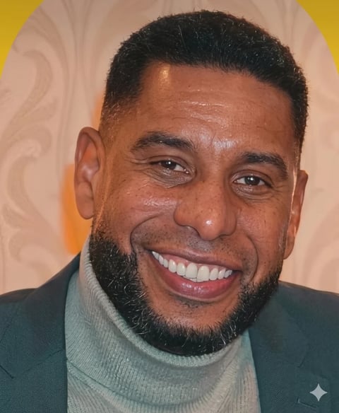 Smiling man with beard wearing dark blazer and gray turtleneck against yellow and beige background